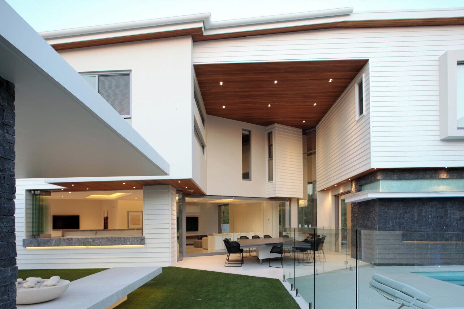 Una casa moderna de dos pisos con comedor, piscina y césped bien cuidado.