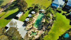 Vista aérea de un resort con una amplia piscina, varias zonas de descanso y exuberante vegetación.