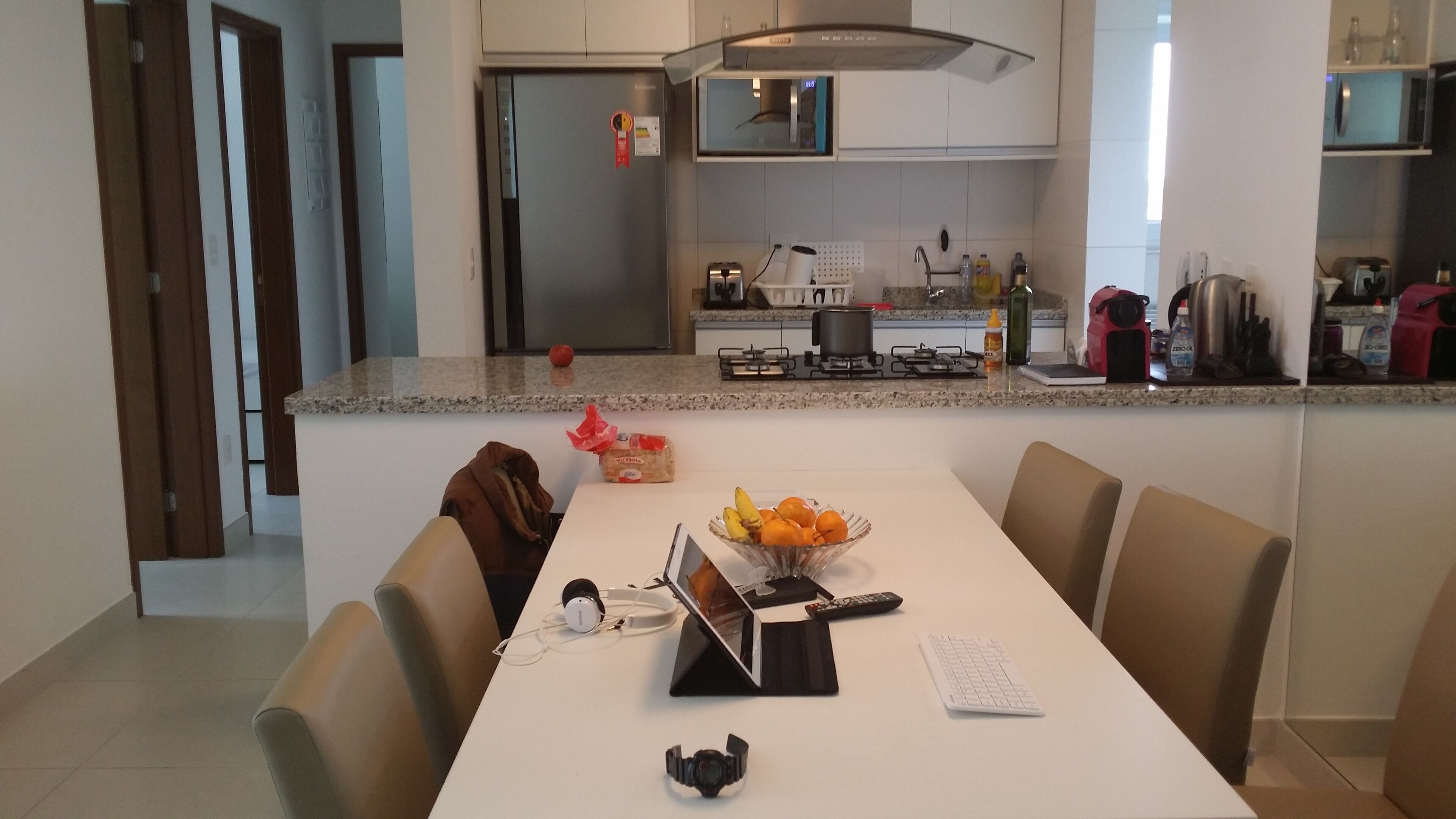 Een moderne keuken met granieten aanrecht, een eethoek met een witte tafel, en een uitzicht op de aangrenzende woonruimte.
