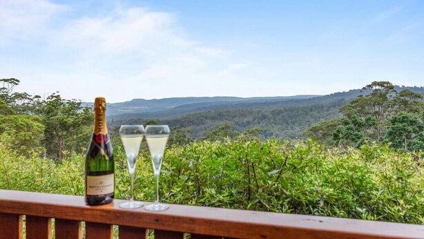 A bottle of Moët & Chandon champagne and two glasses on a wooden railing with a scenic view of a forested landscape. - Quingilli Luxury Chalet 3 Bedrooms (Ravensbourne)