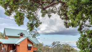 A wooden cabin with a green roof, surrounded by trees and a gravel driveway. - Quingilli Luxury Chalet 3 Bedrooms (Ravensbourne)