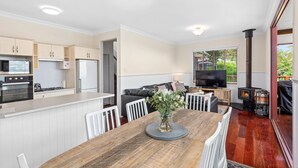 A modern kitchen with white cabinets, a dining area with a wooden table, and a living room with a sofa and TV. - Quingilli Luxury Chalet 3 Bedrooms (Ravensbourne)