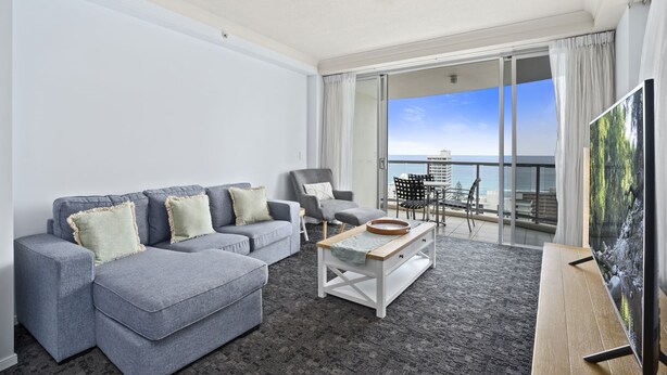 A modern living room with a grey sectional sofa, a white coffee table, and a flat-screen TV on a wooden stand. - Apartment 2196 offers the perfect holiday adobe for small families and couples (Surfers Paradise)