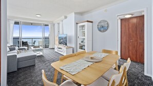 A modern living room with a wooden dining table, grey sofa, and a view of the ocean through large windows. - Apartment 2196 offers the perfect holiday adobe for small families and couples (Surfers Paradise)