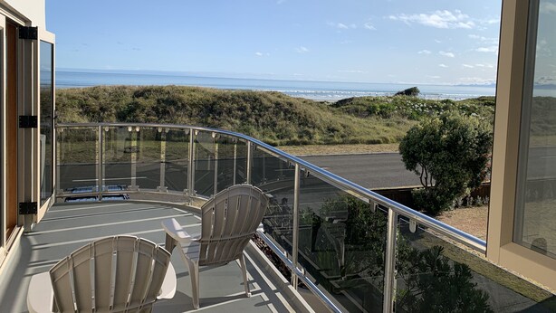 Ein Balkon mit zwei Stühlen und einer Glasreling, der auf eine Küstenlandschaft mit Vegetation und Meerblick blickt.
