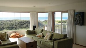 Ein modernes Wohnzimmer mit einem großen grünen Sofa, einem Holztisch und Blick auf den Ozean durch raumhohe Fenster.