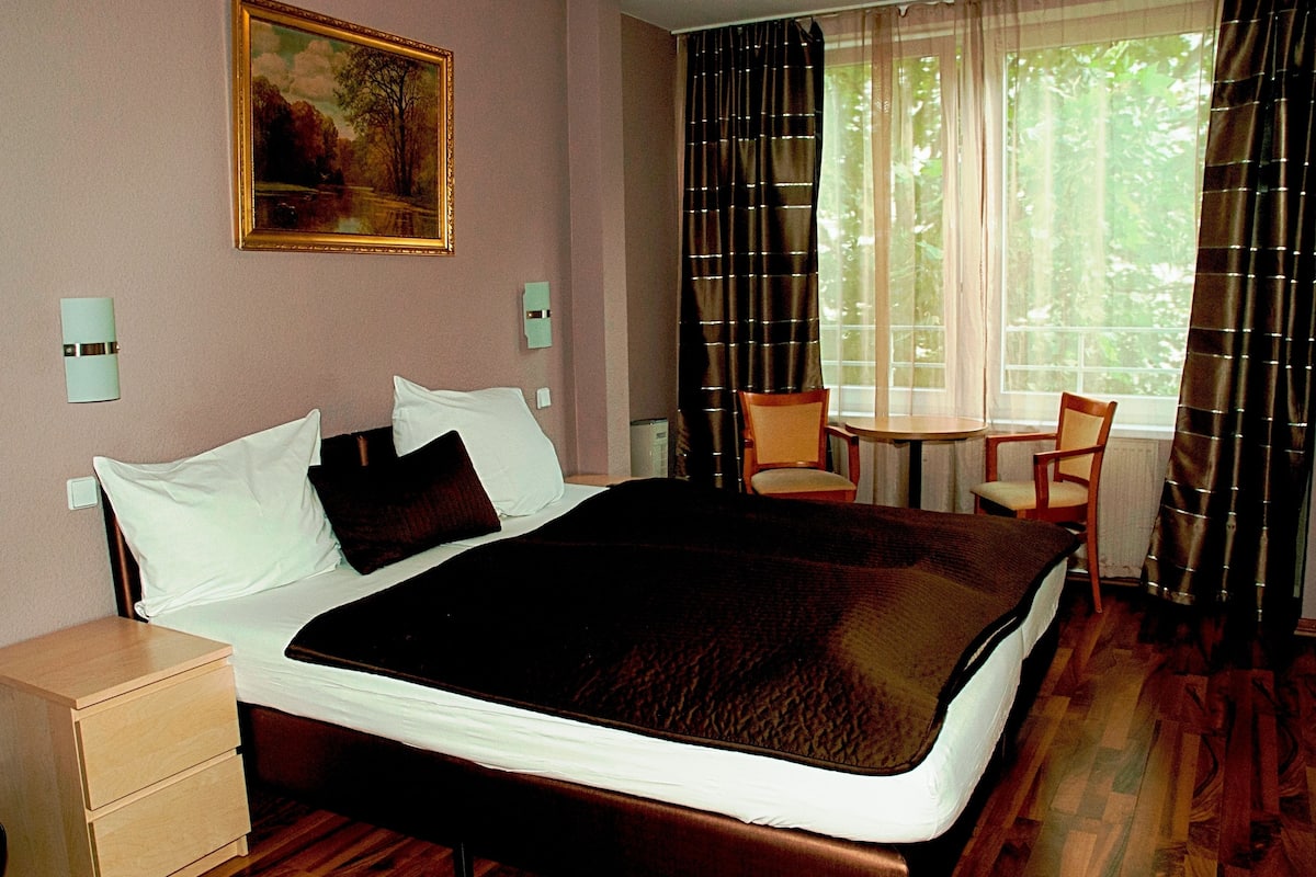 A hotel room with a large bed, a small table, two chairs, a nightstand, and a painting on the wall.