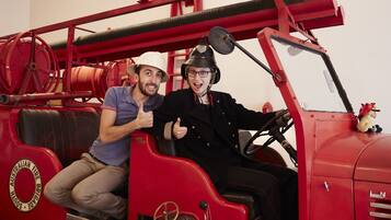 Zwei Personen in einem Oldtimer-Feuerwagen mit erkennbarer Beschriftung und Schlauchaufroller.