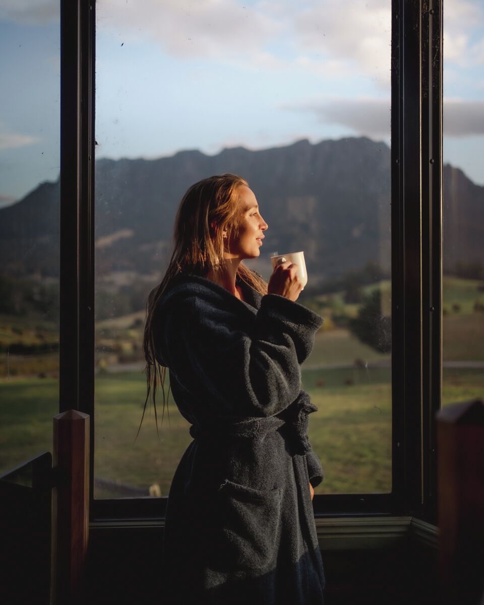 Una persona con bata junto a una ventana con vistas a las montañas.