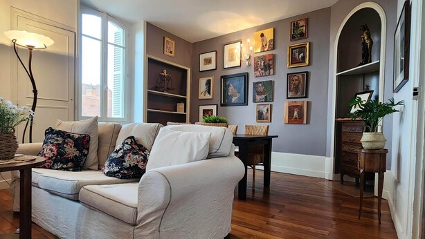 Una sala de estar con un sofá blanco, piso de madera y una pared decorada con obras de arte enmarcadas.