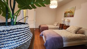 Un dormitorio con dos camas, una planta grande en maceta, una cesta tejida y un cuadro en la pared.