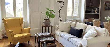Una sala de estar con un sillón amarillo, un sofá blanco, una mesita y una planta en maceta.