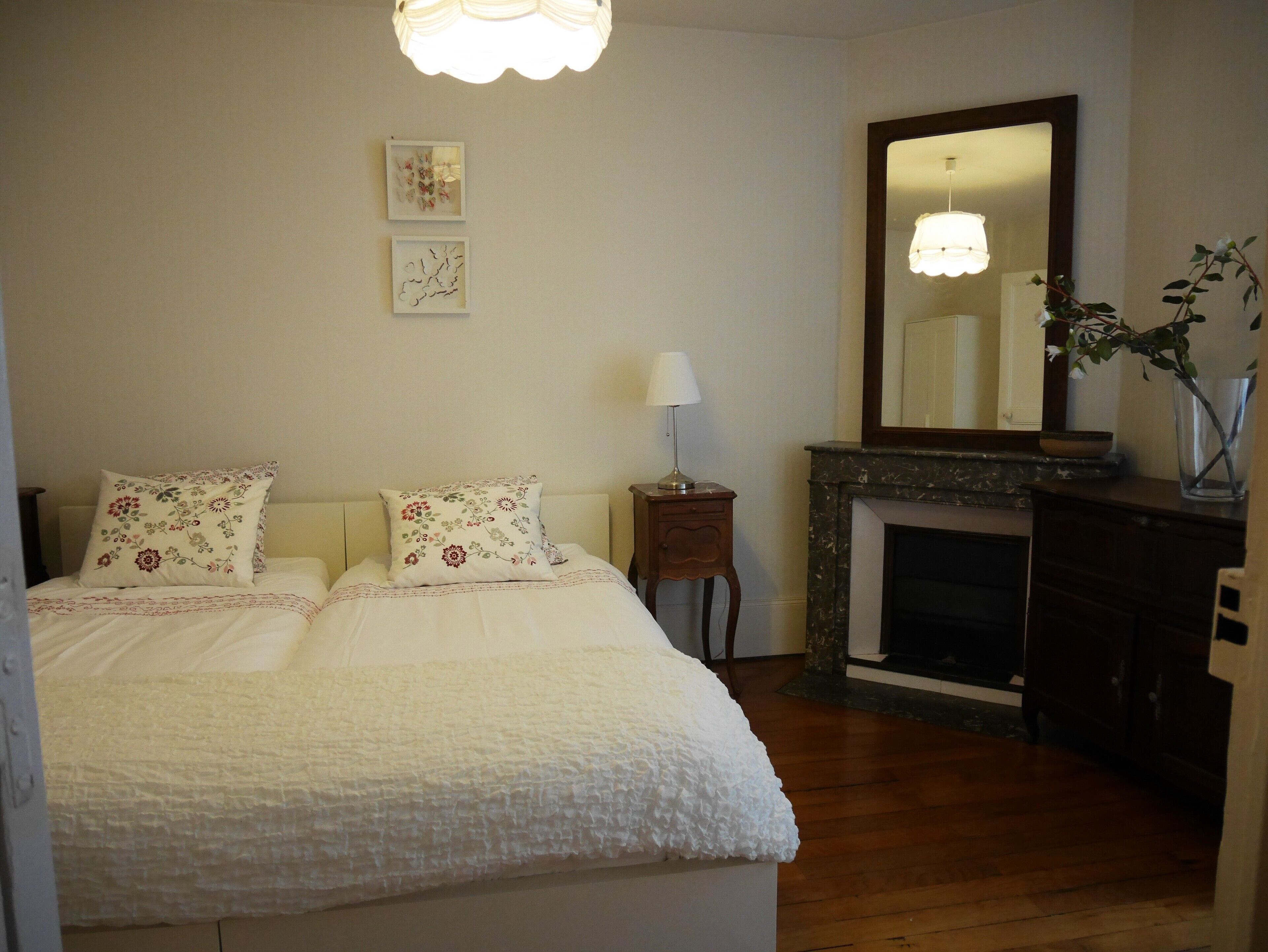 Un dormitorio con cama, mesita de noche, espejo y chimenea.