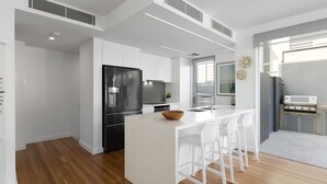 Cozinha moderna com ilha central, banquetes brancos, eletrodomésticos de aço inoxidável e vista para o exterior.