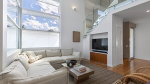 Uma sala de estar moderna com um sofá seccional, uma televisão de tela plana e uma escada que leva a um andar superior.