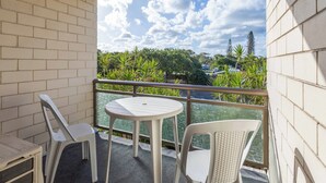 A balcony with a white table and two chairs, overlooking a lush green landscape and a body of water. - Two Bedroom Apartment - Unit 4 Foreshores (Sunshine Coast)