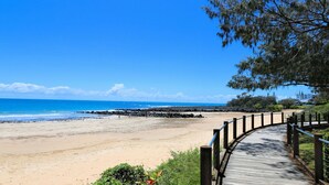 Une promenade en bois qui mène à une plage, d’où l’on a une vue dégagée sur l’océan et les bâtiments situés au loin.