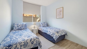 A bedroom with two beds, a window, a bedside table, and a framed picture on the wall. - HEADLANDS 2: 2  BR, 1  BA Apartment in Port Macquarie, Sleeps 4 (Port Macquarie)