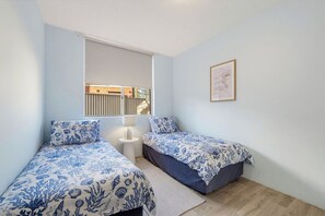 A bedroom with two beds, a window, a bedside table, and a framed picture on the wall. - HEADLANDS 2: 2  BR, 1  BA Apartment in Port Macquarie, Sleeps 4 (Port Macquarie)