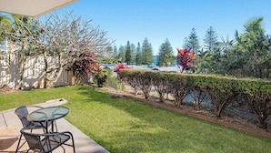 A patio area with a table and chairs, a well-maintained lawn, and a variety of trees and shrubs. - HEADLANDS 2: 2  BR, 1  BA Apartment in Port Macquarie, Sleeps 4 (Port Macquarie)