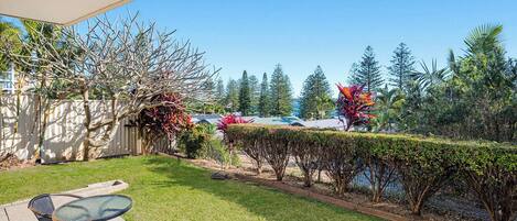 A patio area with a table and chairs, a well-maintained lawn, and a variety of trees and shrubs.