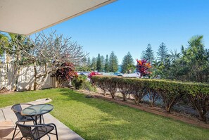 A patio area with a table and chairs, a well-maintained lawn, and a variety of trees and shrubs. - HEADLANDS 2: 2  BR, 1  BA Apartment in Port Macquarie, Sleeps 4 (Port Macquarie)