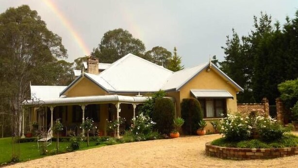 Une maison à deux étages, dotée d’un toit à pignon bien visible, d’un porche abrité et d’un jardin bien entretenu où poussent diverses plantes et fleurs.
