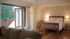 Une chambre à coucher avec un lit en bois, deux lampes de chevet, une tête de lit en bois et une vue sur un balcon extérieur accessible par une porte-fenêtre coulissante.