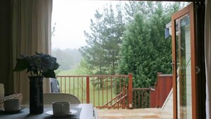 Une pièce donnant sur une terrasse en bois et une porte menant à un jardin. On y trouve une table avec un vase de fleurs et une tasse.