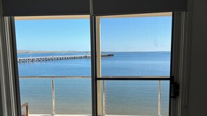 Ein Zimmer mit einer großen Schiebetür, die auf einen Balkon mit Blick aufs Meer und einen Steg führt.