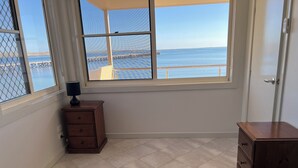 Ein Schlafzimmer mit zwei Betten, einem Fenster mit Blick auf das Meer und einen Steg, einer Holzkommode und einer Tür.
