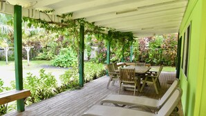 A covered patio with a wooden deck, a table with chairs, and a lounge chair. - Tuteveras' Arms - Arorangi (Arorangi)