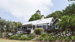 A modern house with a large deck, surrounded by lush greenery and flowering plants.