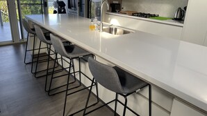A modern kitchen with a large island, bar stools, a stainless steel sink, and a view of the outdoors.