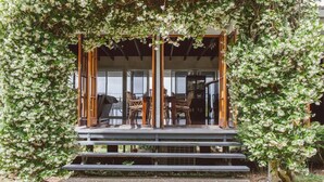 A covered outdoor seating area with wooden chairs and tables, surrounded by lush greenery.