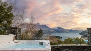 Un bain à remous avec un mur en pierre et une vue sur les montagnes et un lac.