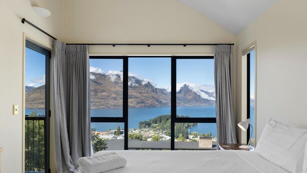 Une chambre avec un grand lit, une vue sur un lac et des montagnes, et un balcon avec des rideaux.