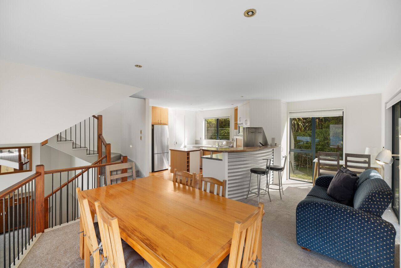 A modern kitchen with a central island, a dining area with a wooden table and chairs, and a living area with a sofa and a TV.