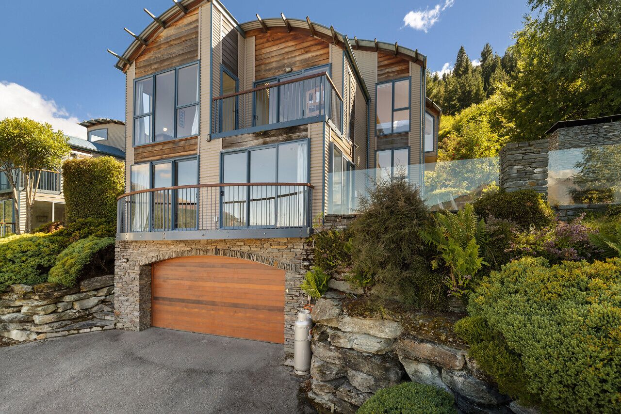 Una casa moderna de varios pisos con fachada de piedra, ventanas grandes y puerta de garaje de madera.