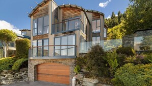 Une maison moderne à plusieurs étages, dotée d’une façade en pierre, de grandes fenêtres et d’une porte de garage en bois.