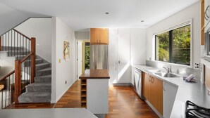 Une cuisine moderne avec un îlot central, un escalier en bois et de grandes fenêtres.