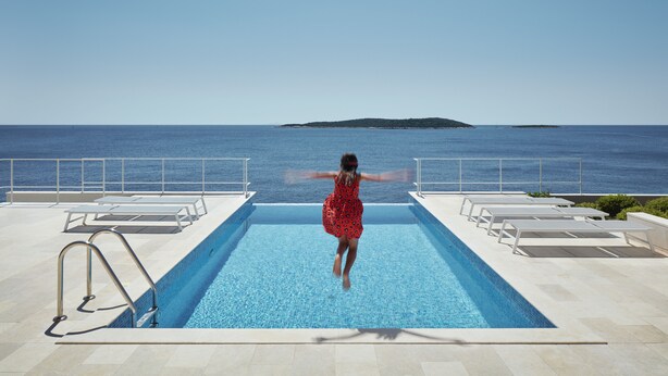 A pool with a view of the sea, lounge chairs, and a woman jumping into the pool. - A Place Where The Garden Ends And The Sea Begins (Milna)