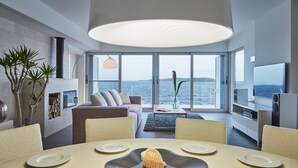A modern living room with a large window, a fireplace, and a dining area with a table set for two. - A Place Where The Garden Ends And The Sea Begins (Milna)