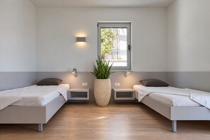 A modern room with two beds, a large potted plant, and a window with a view of greenery. - A Place Where The Garden Ends And The Sea Begins (Milna)