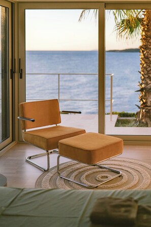 Una stanza con vista sul mare, una sedia, un tavolino e un letto.