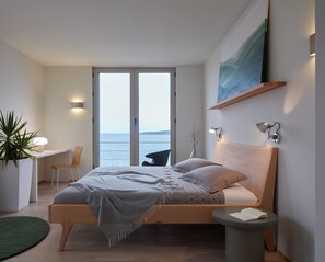 A modern bedroom with a bed, bedside table, and a view of the sea.