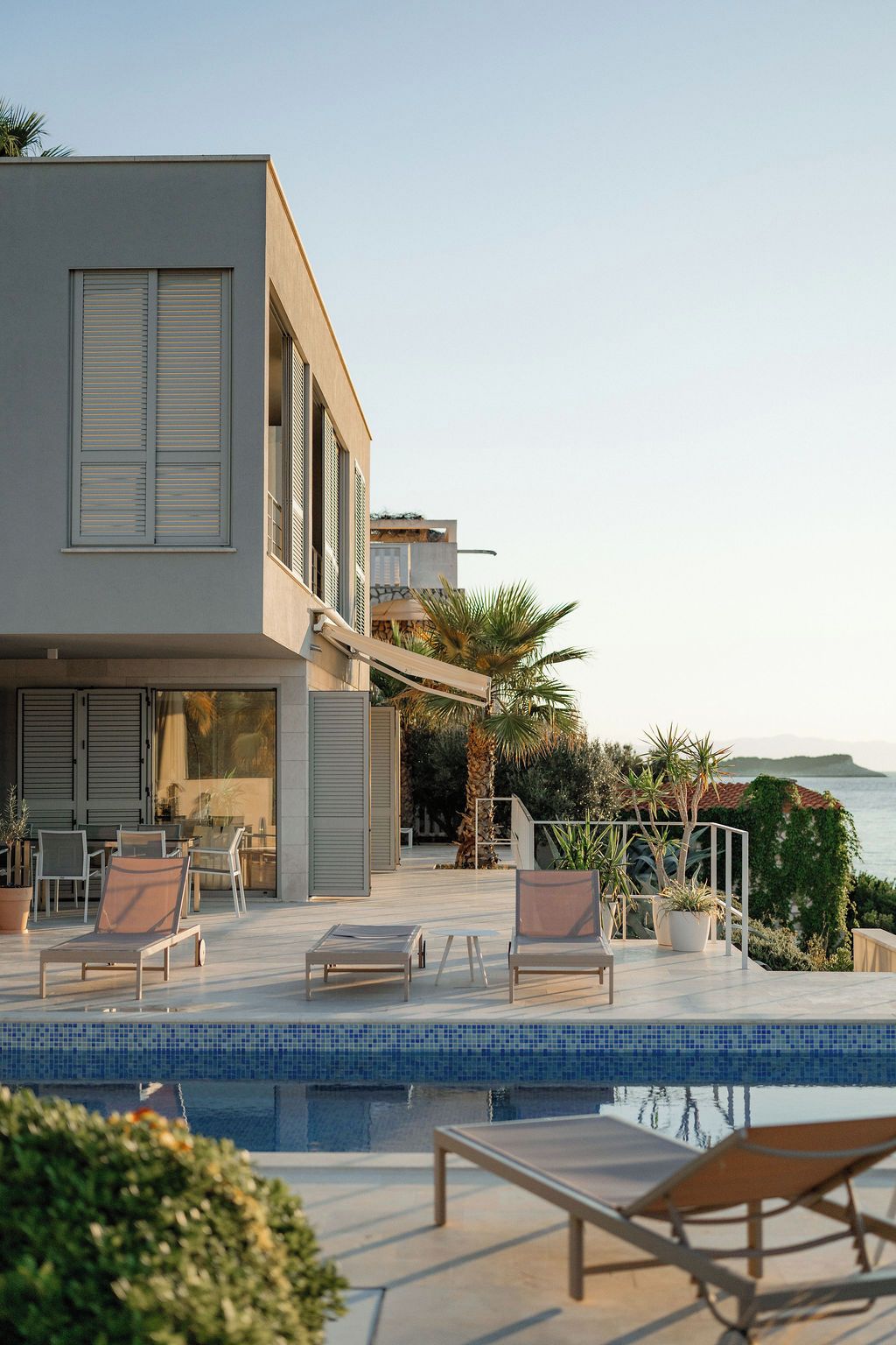 A modern building with a pool area, outdoor seating, and a view of the sea.