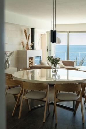 Un'area pranzo moderna con un tavolo rotondo, sedie in legno e vista sul mare.