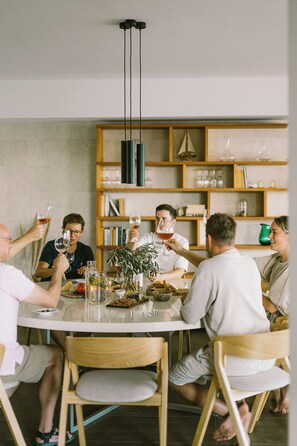 A group of people sitting around a round table with a bottle of wine, glasses, and a plant centerpiece.