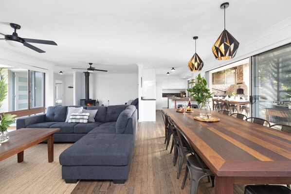 Un salon moderne avec un canapé d’angle, une table à manger en bois et une cuisine en arrière-plan.